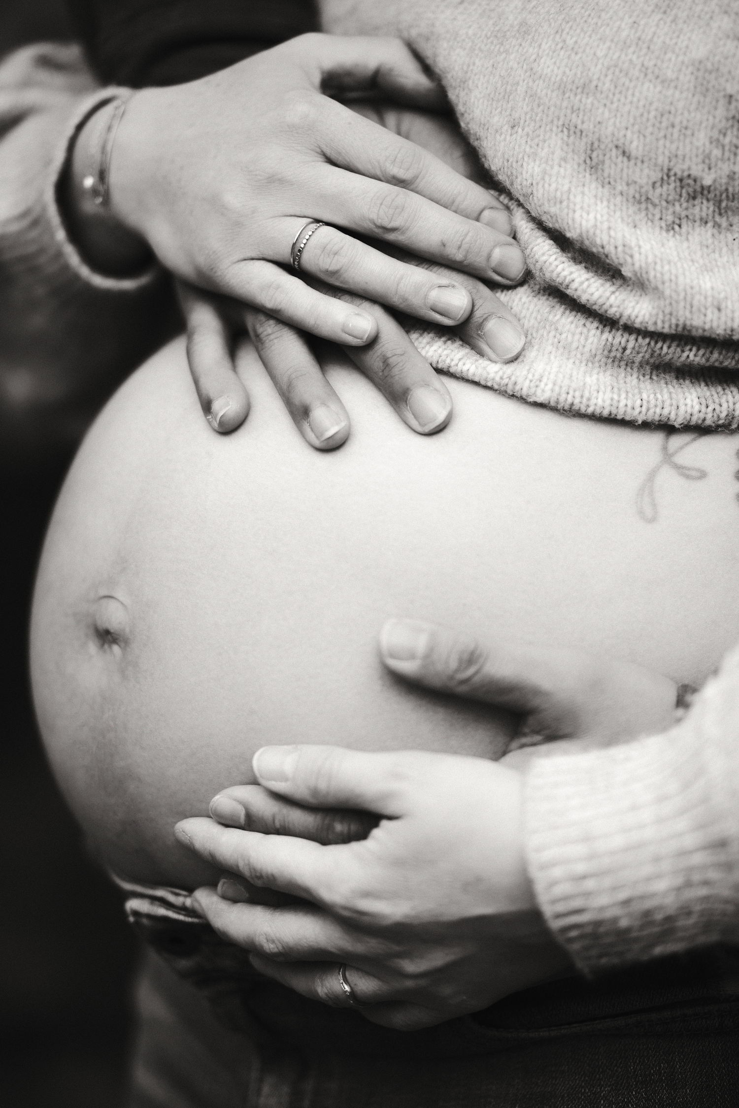 Black and white close-up of hands gently cradling a pregnant belly.