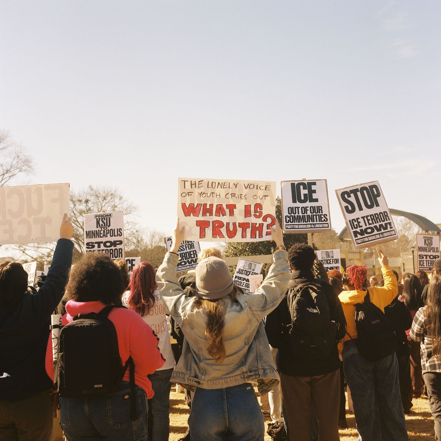 Protesters hold signs demanding truth and justice while demonstrating in a line at an outdoor rally.
