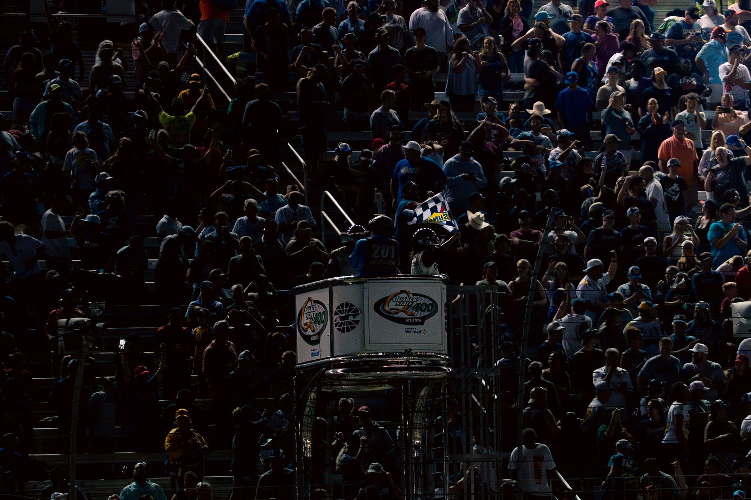 Crowded spectator stands at motorsport event photographed in low light conditions.