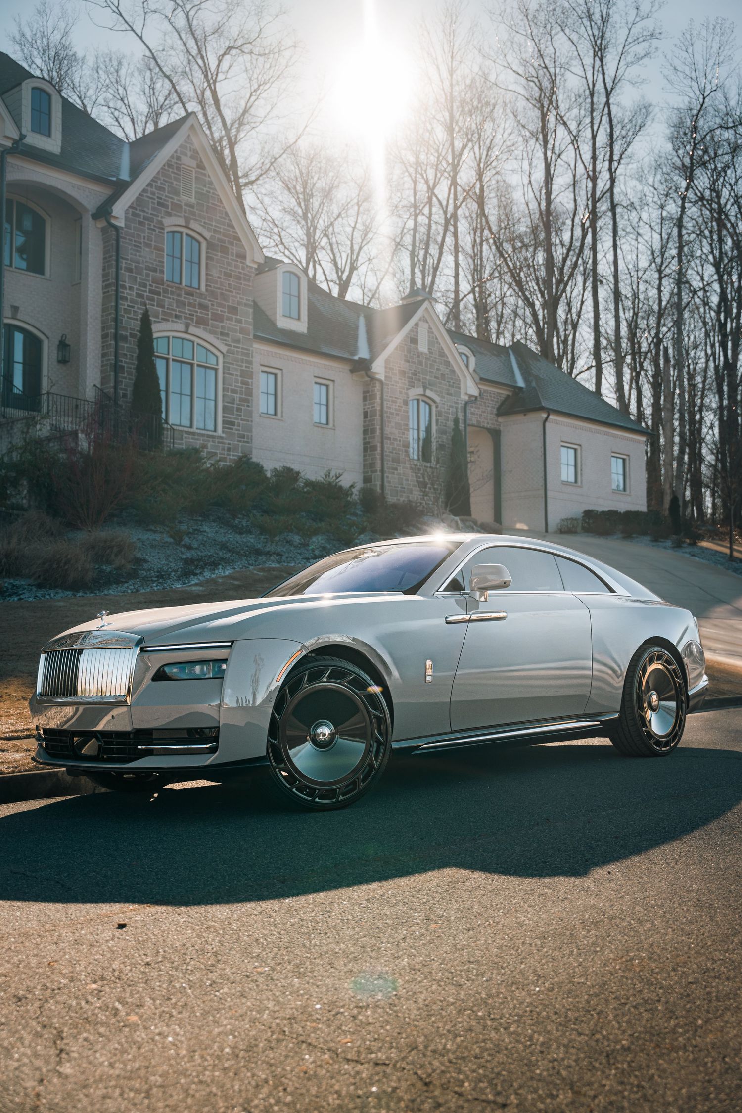 A sleek silver Lincoln luxury car parked on a driveway with dramatic sunlight and trees in the background.