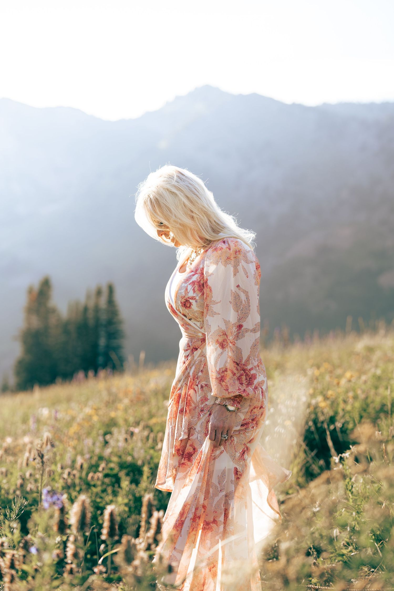 Person in a floral dress walking through a mountain meadow at golden hour.