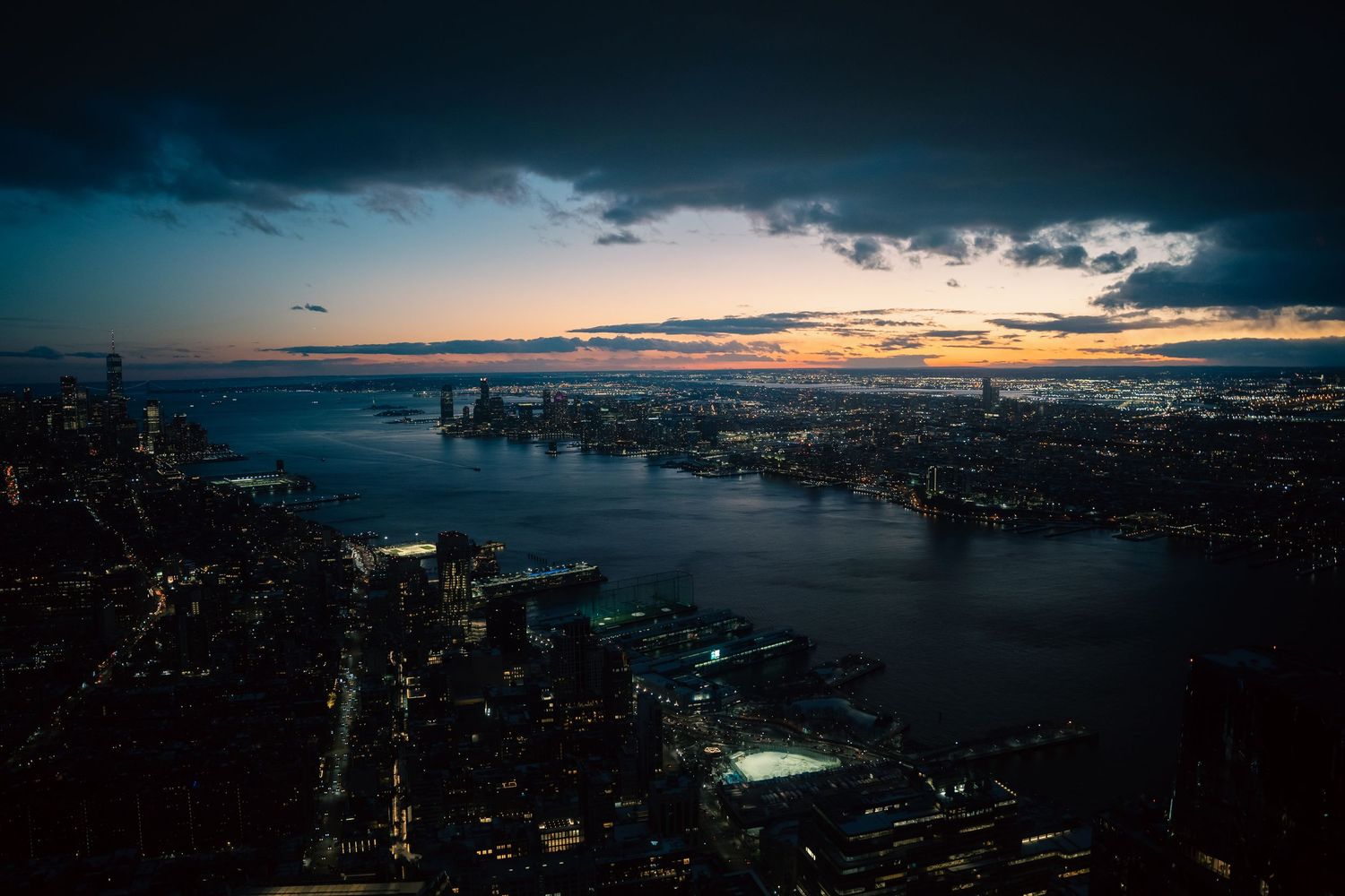 Panoramic cityscape at dusk showing harbor and urban skyline.