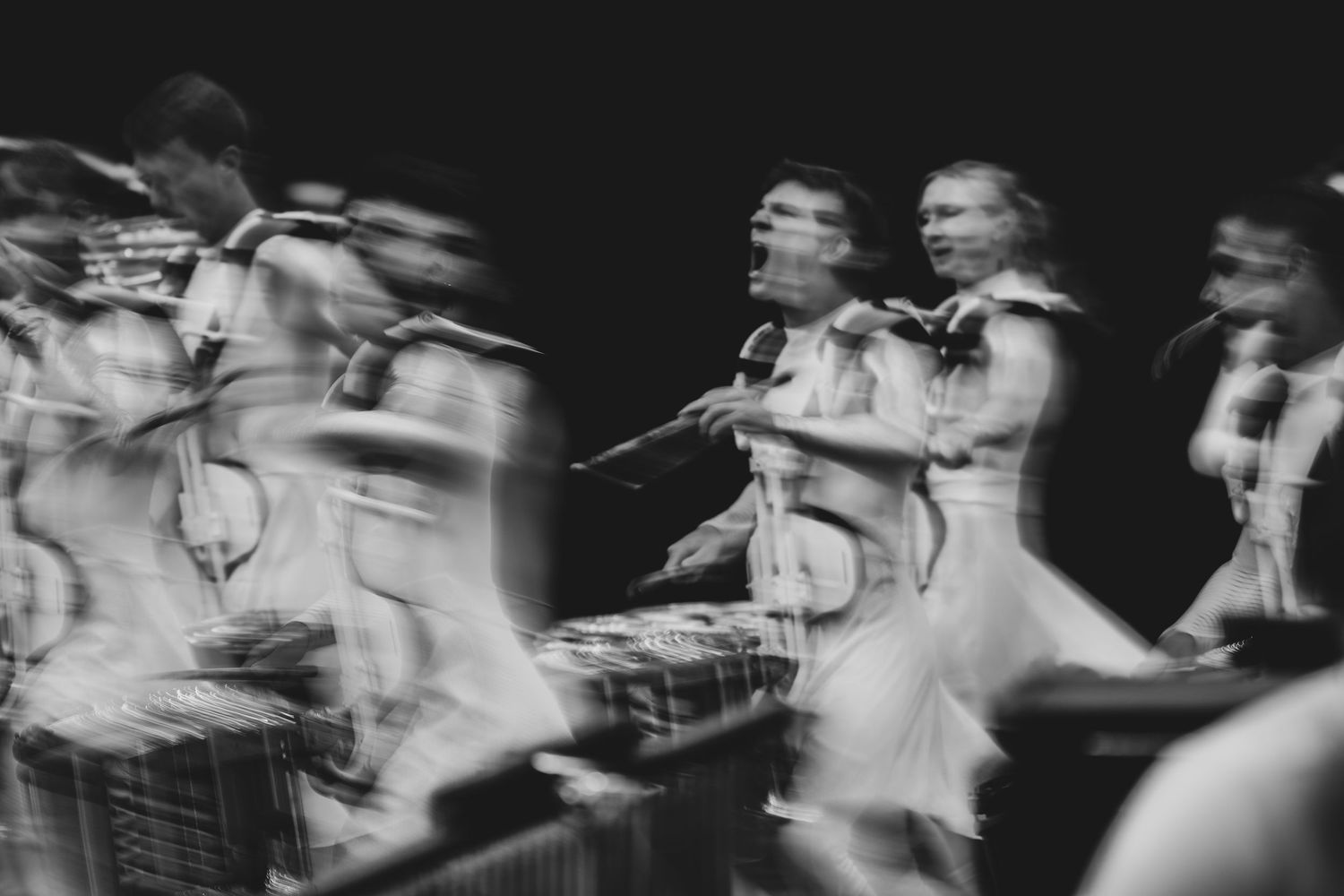 Blurred black and white photo of musicians performing, capturing dynamic motion during a live orchestral concert.