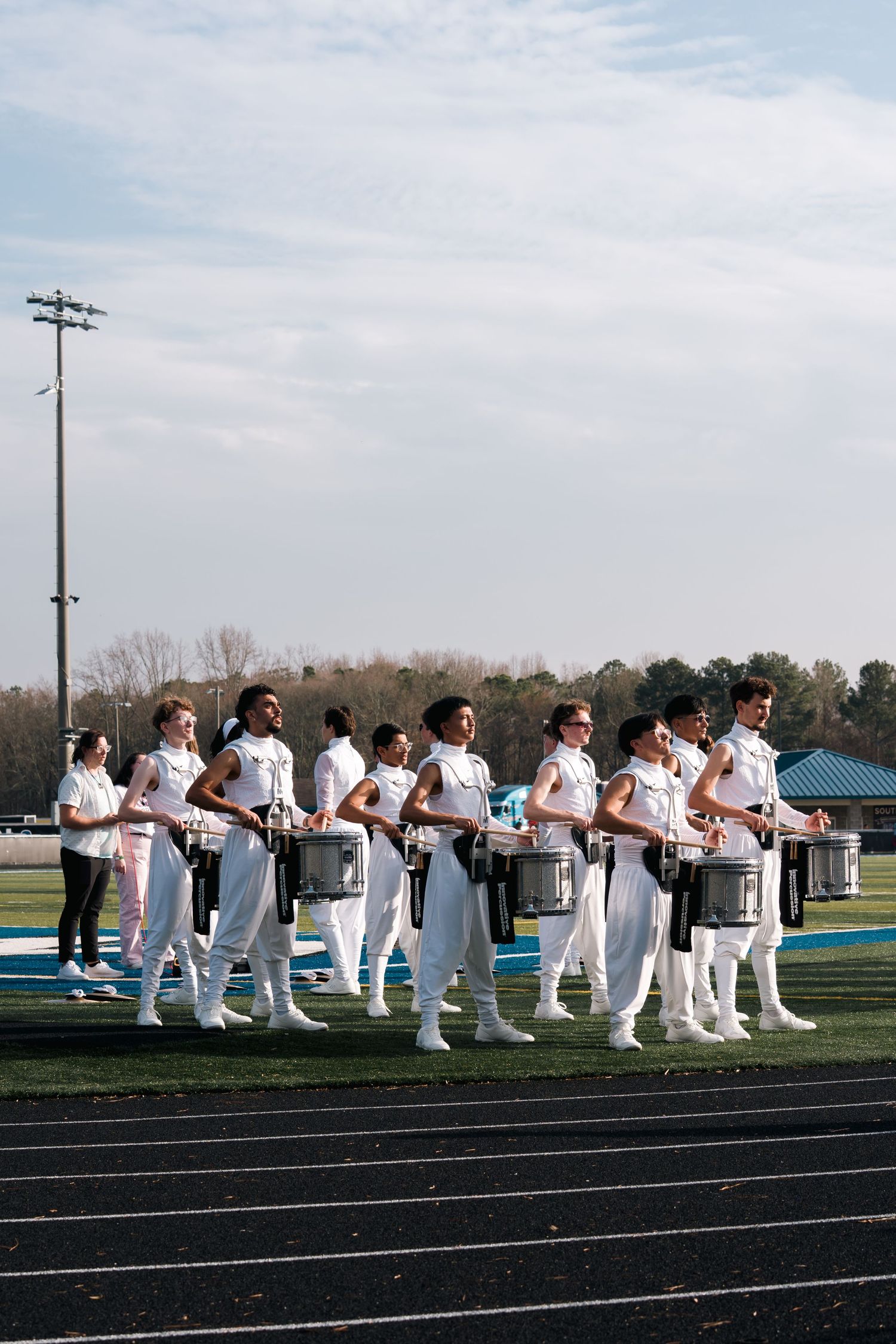 Row of athletes in white uniforms kneeling on a track field during a sports event.