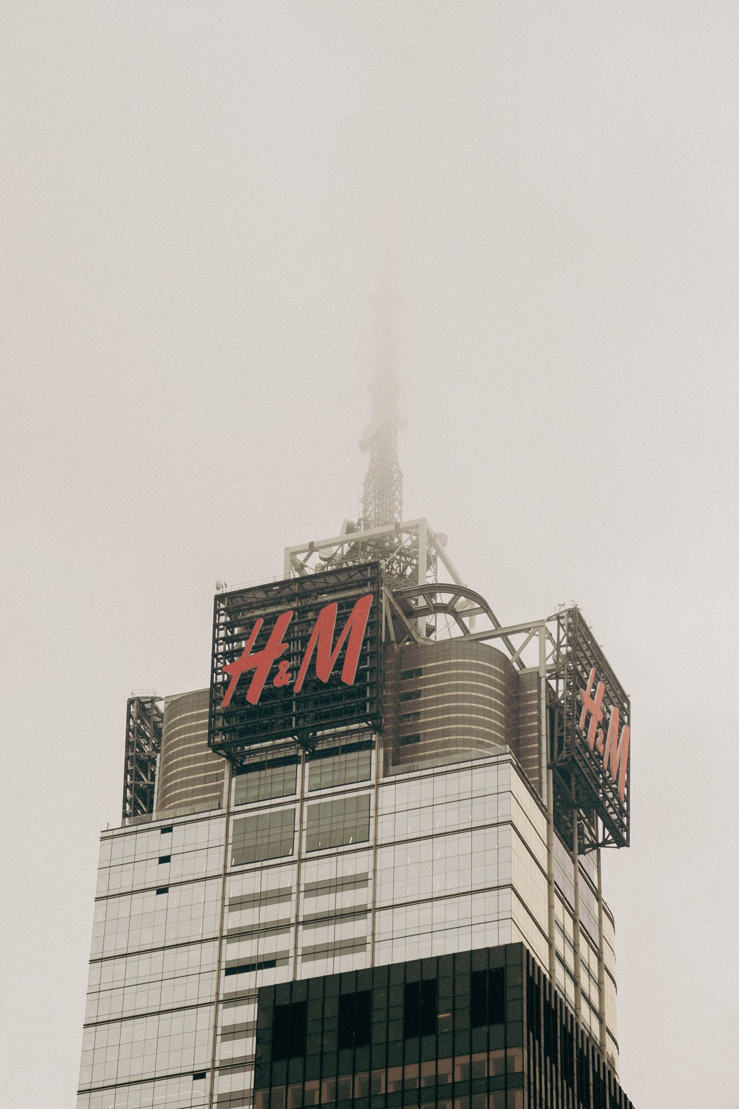 H&M store sign on top of modern building facade disappearing into foggy sky.