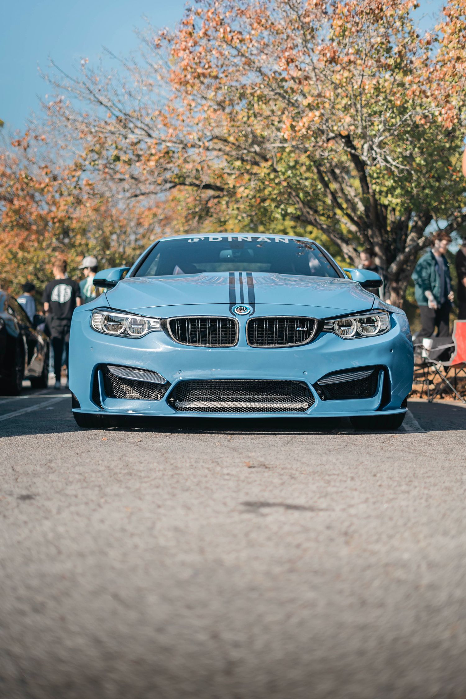 Light blue BMW M4 photographed low to the ground with autumn trees in the background.