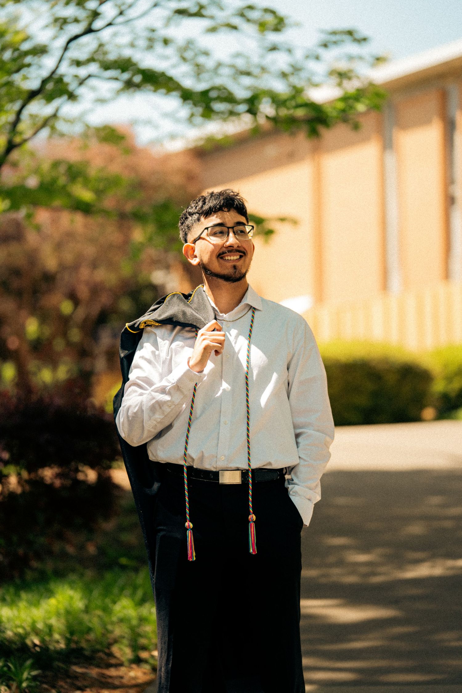 Person in formal attire posing in golden sunlight near brick building.