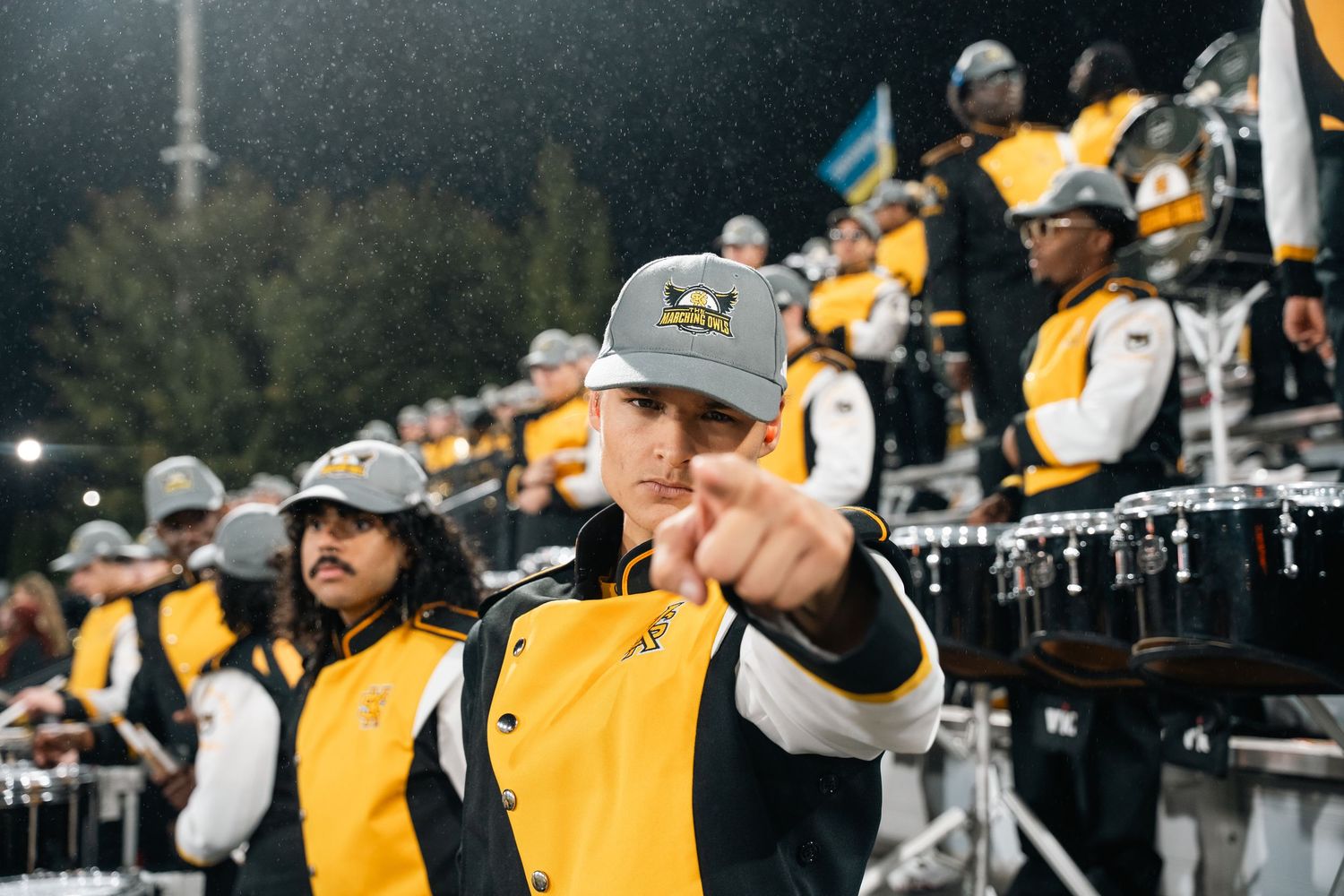 Marching band members in formation wearing yellow and black uniforms during outdoor performance.