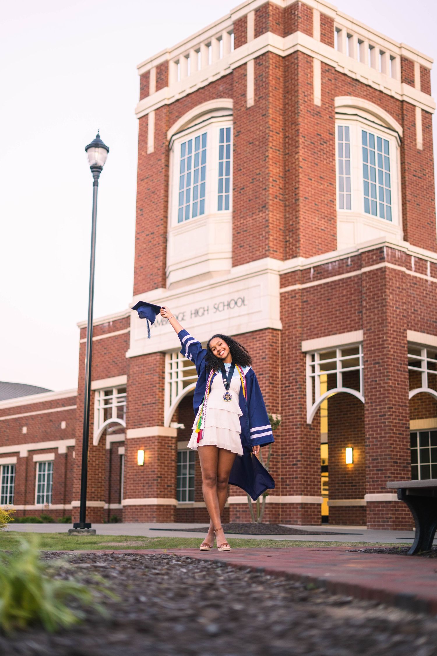 Graduate celebrating in front of brick university building with cap toss.