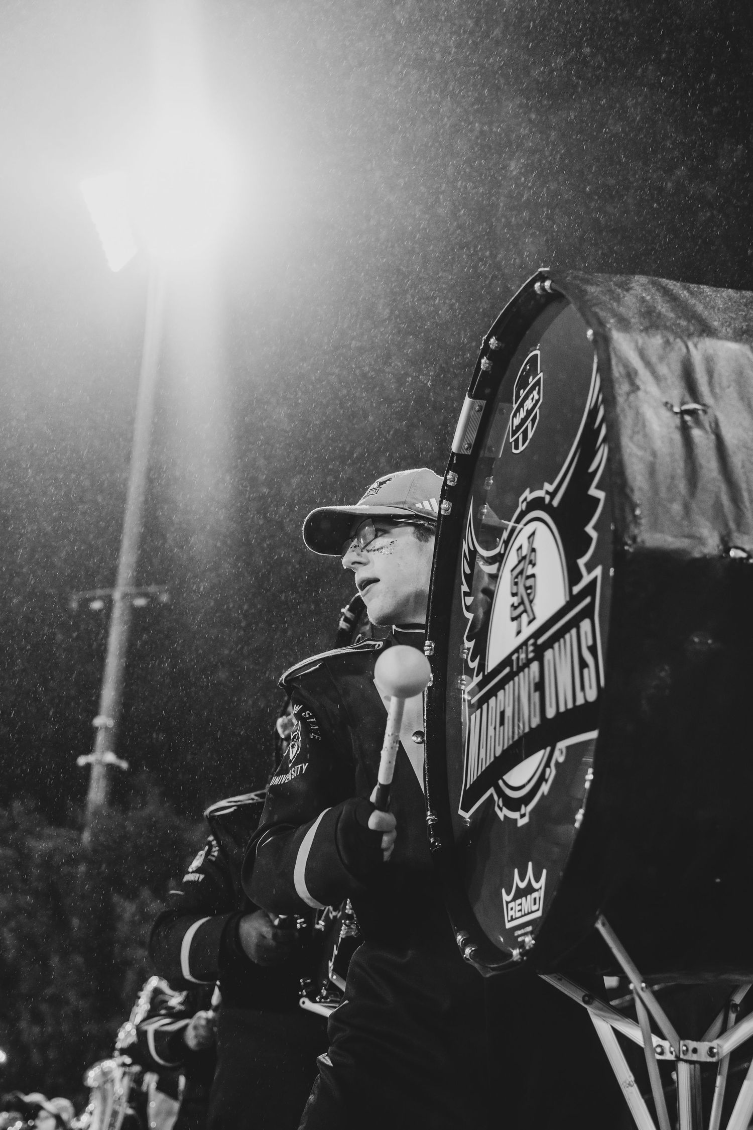 Marching band conductor leads performers during nighttime performance in black and yellow uniforms.