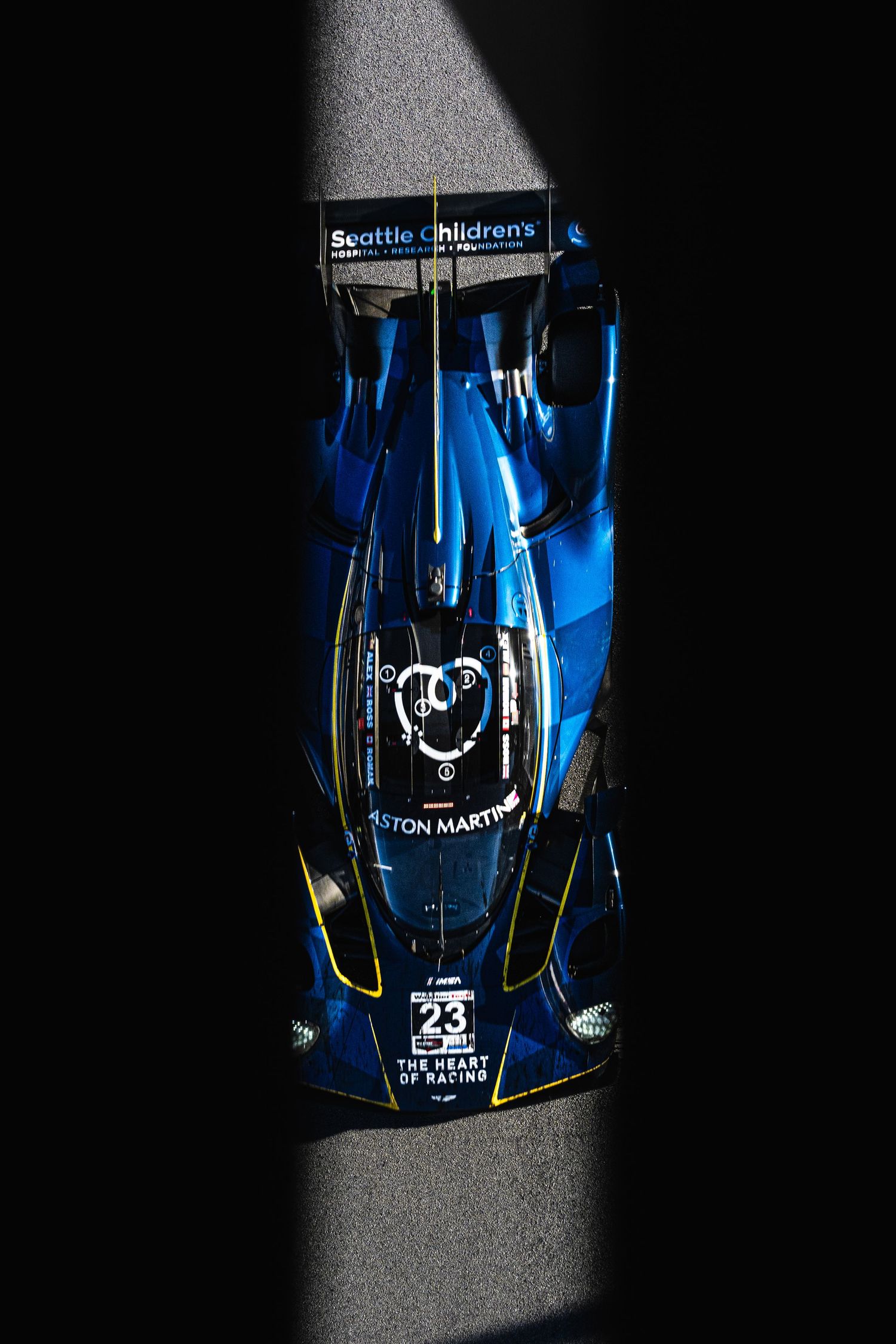 Close-up view of blue Aston Martin racing car with number 23 on black background.