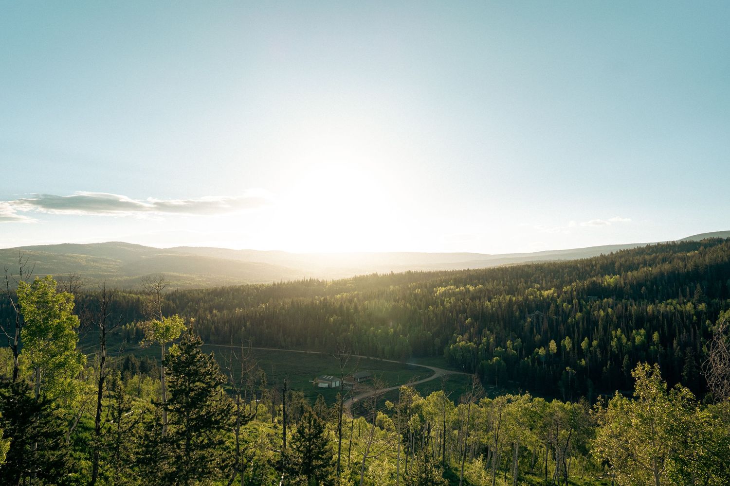 Panoramic mountain vista with evergreen forests and sunlight breaking through clouds.
