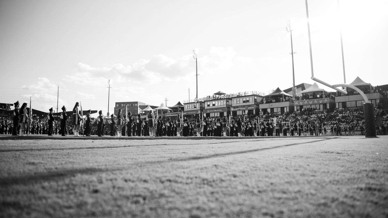 Minimalist panoramic landscape showing a distant crowd gathered on a vast empty field.