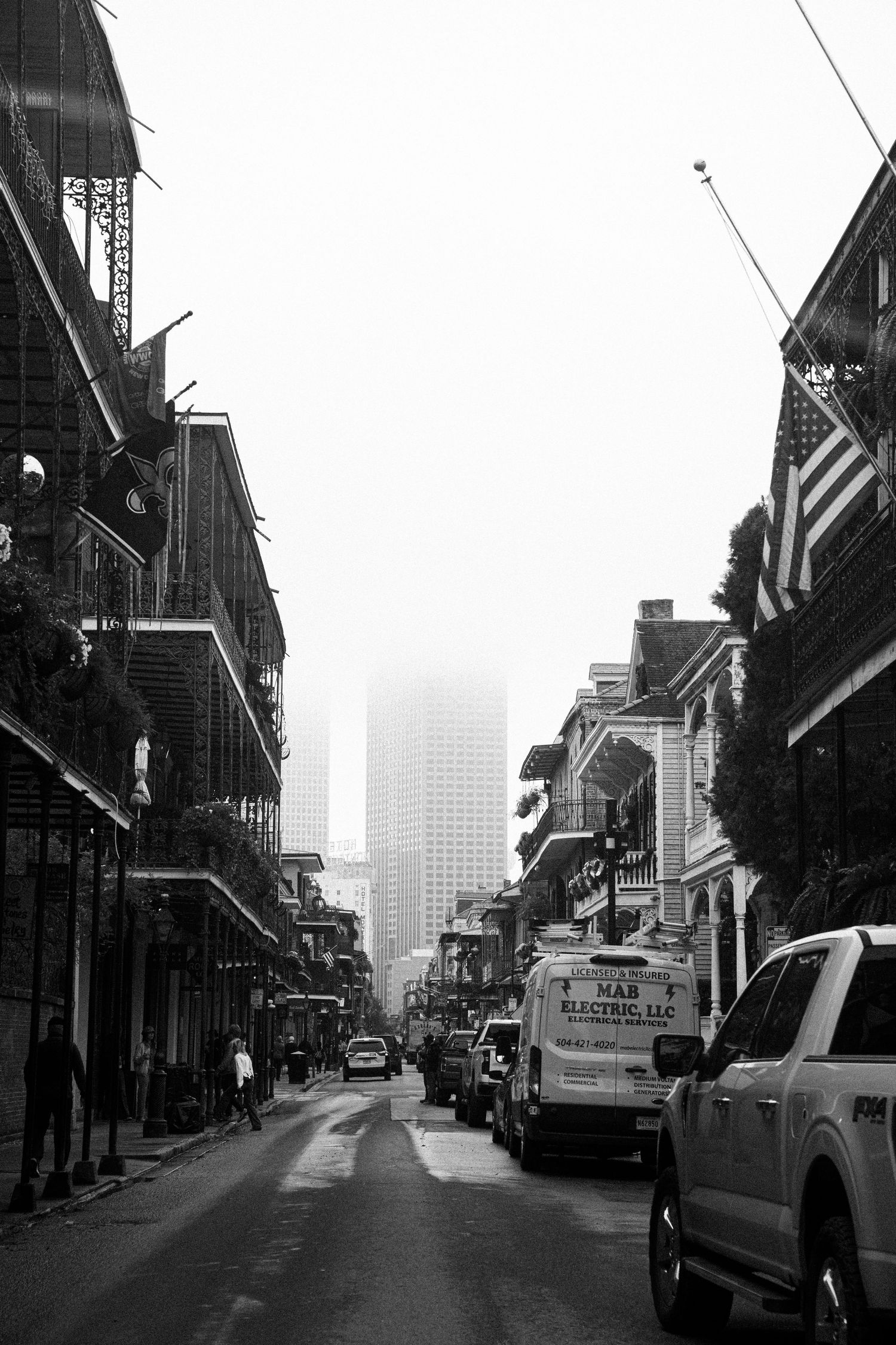 Foggy street scene in New Orleans French Quarter with parked vehicles and historic buildings.