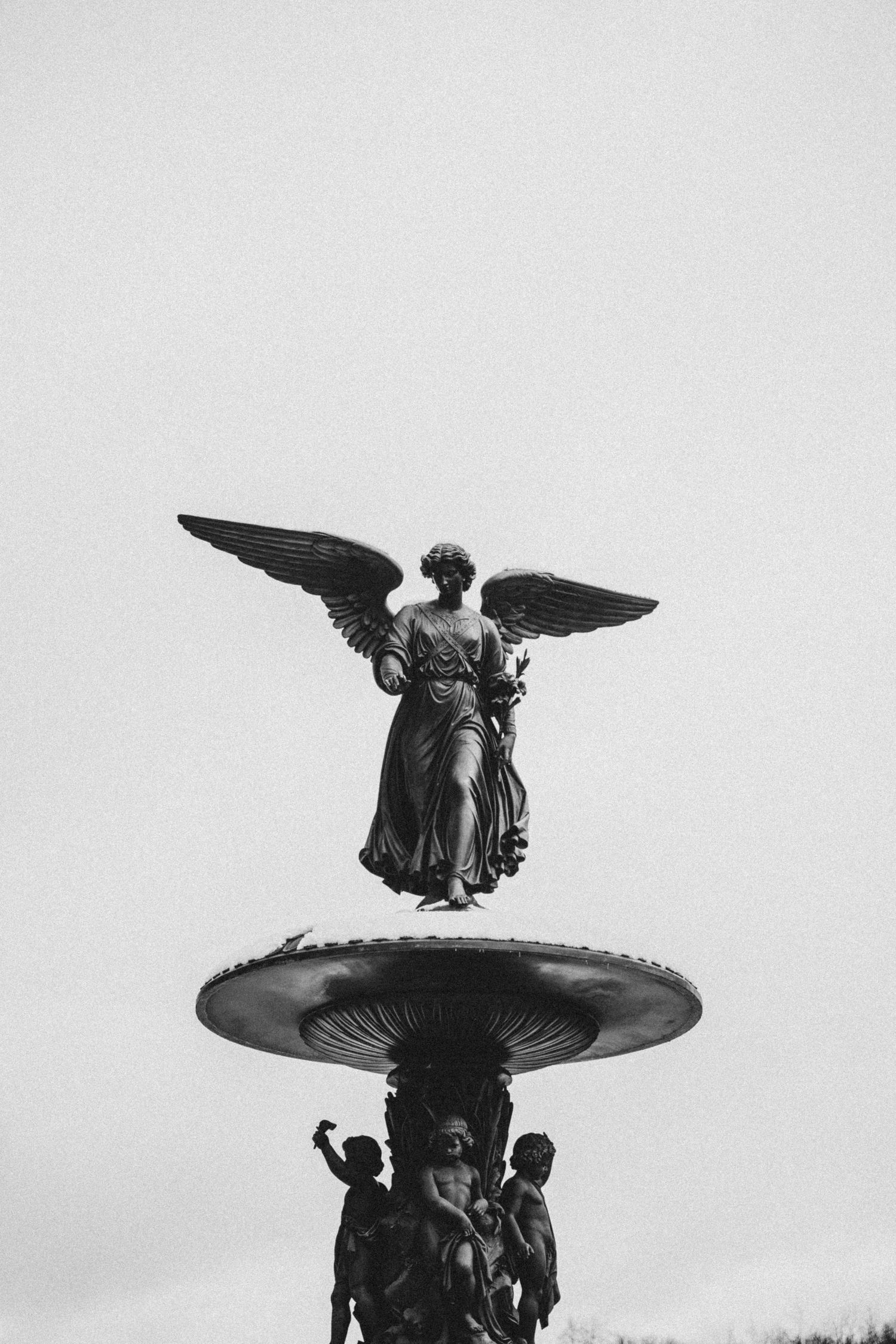 Ornate angel statues with spread wings adorn the top of a classical fountain structure in a public square.