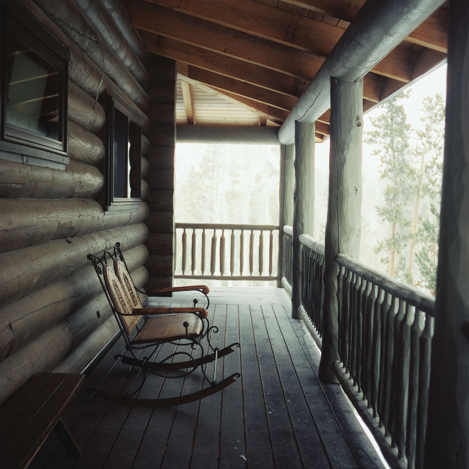 Rustic log cabin porch with rocking chairs and wooden railings in shadow.