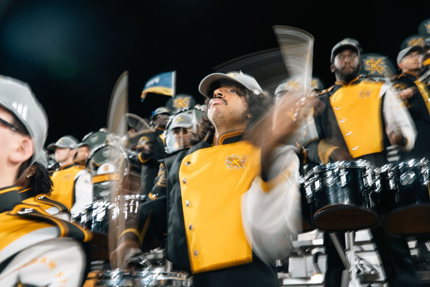 Marching band performers in yellow uniforms create dynamic formations during field show.