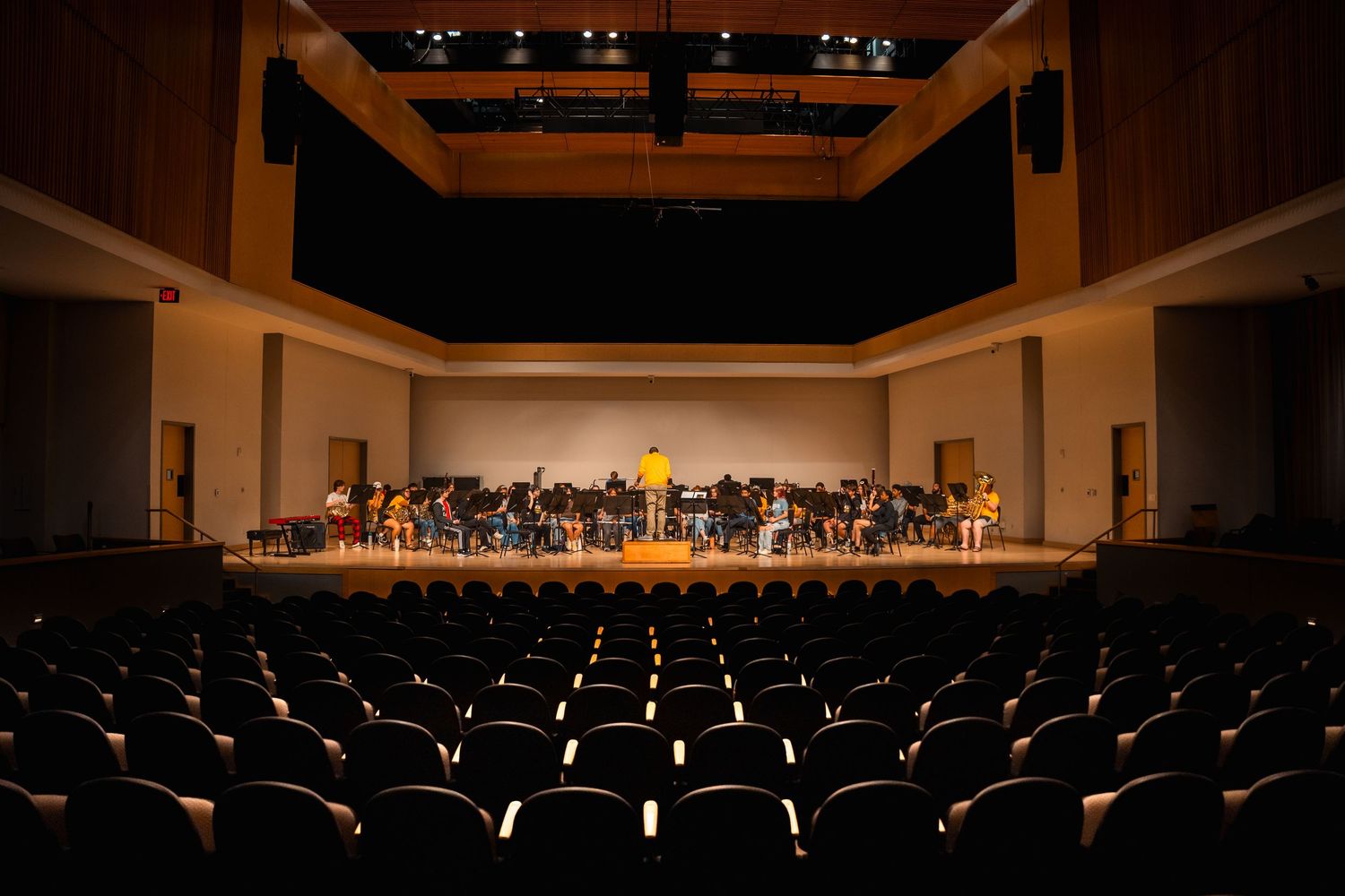 Empty concert hall with rows of seats facing an illuminated stage with performers.