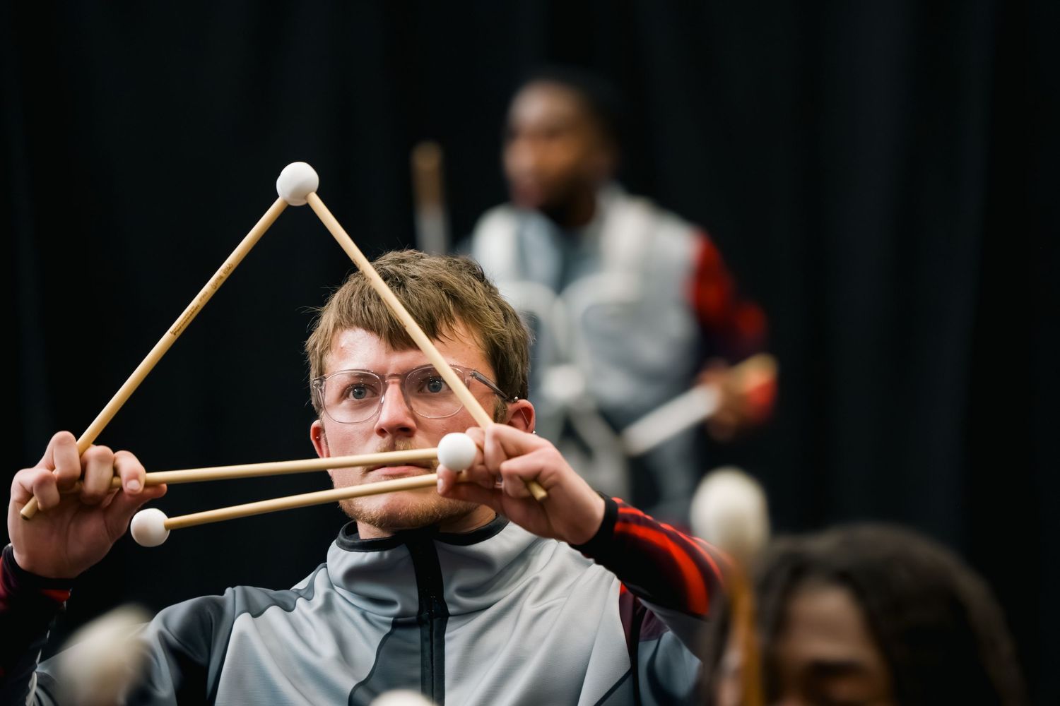 Young musician holds multiple drumsticks in an X formation during a marching percussion ensemble rehearsal.