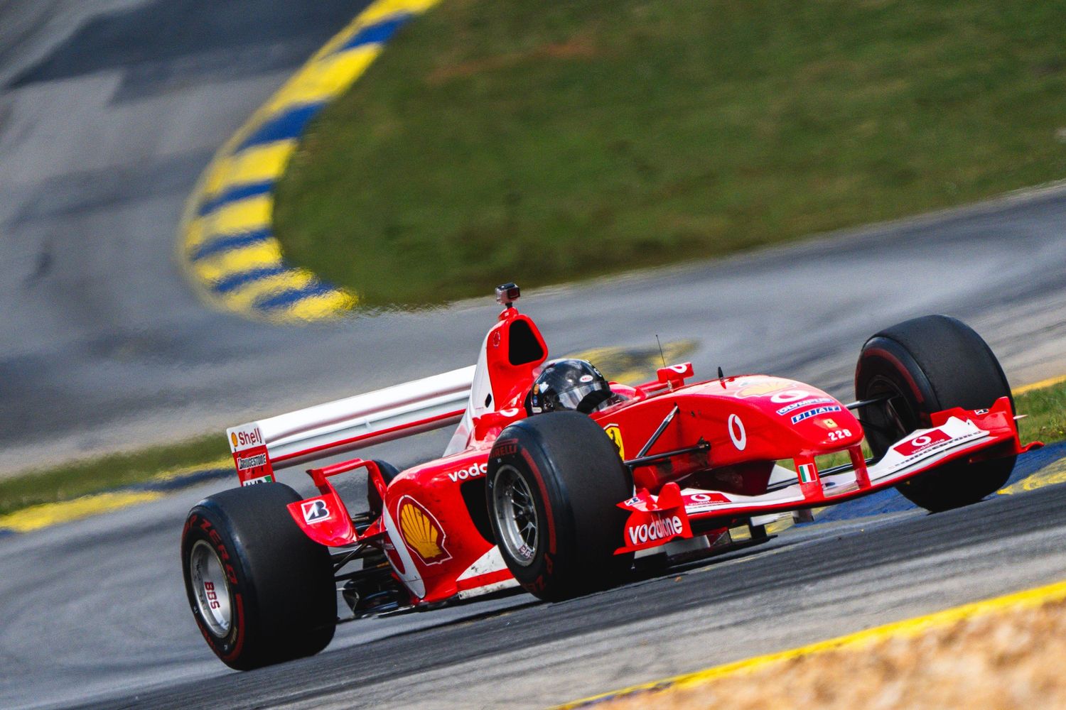 Red Ferrari Formula 1 race car speeding around a curved track during a sunny motorsport racing event.
