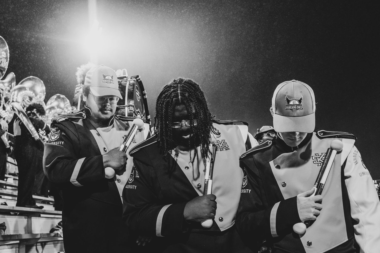 Black and white photograph of marching band members performing in dramatic lighting.