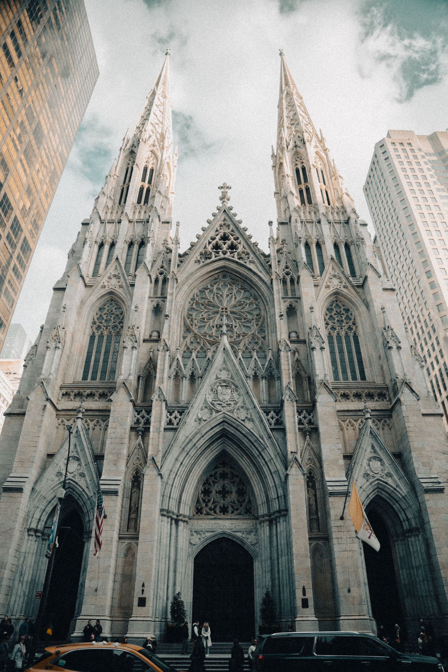 Gothic spires and arches of St. Patrick's Cathedral rise against a cloudy New York City sky.
