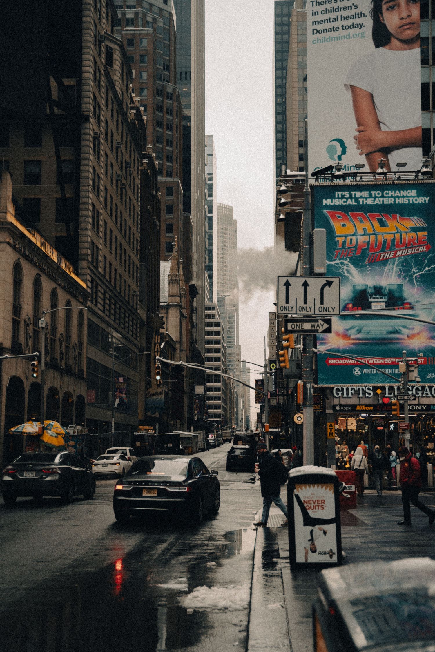 Rainy city street with vintage cars and movie posters on buildings in dark moody lighting.