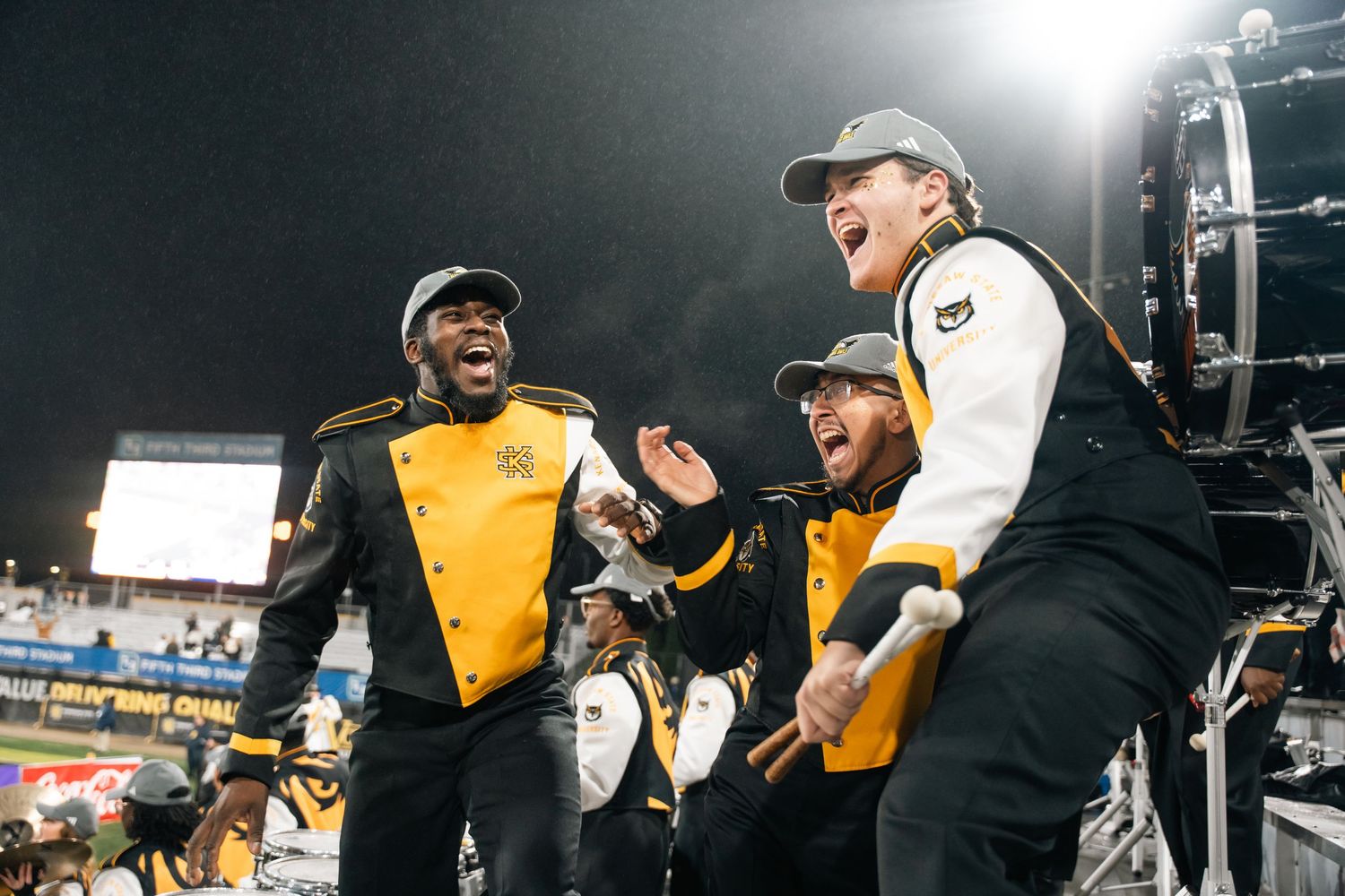 Band members in yellow and black uniforms perform during nighttime event.