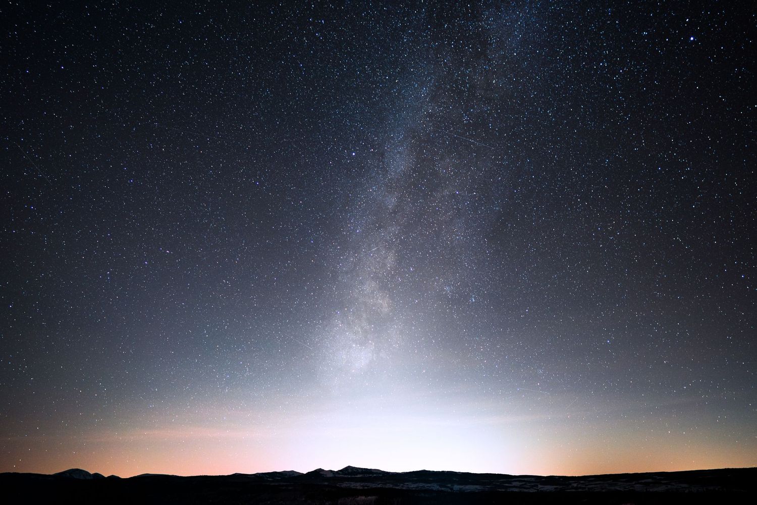 Stunning night sky panorama showing the Milky Way galaxy over dark mountain silhouettes.