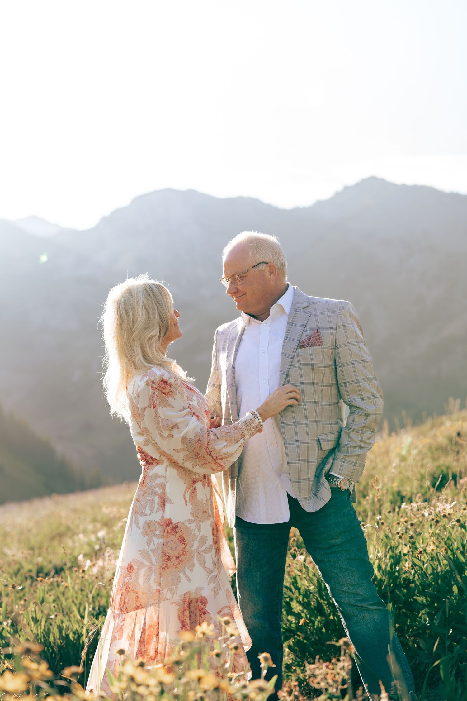 Romantic couple embraces in a mountain meadow during golden hour.