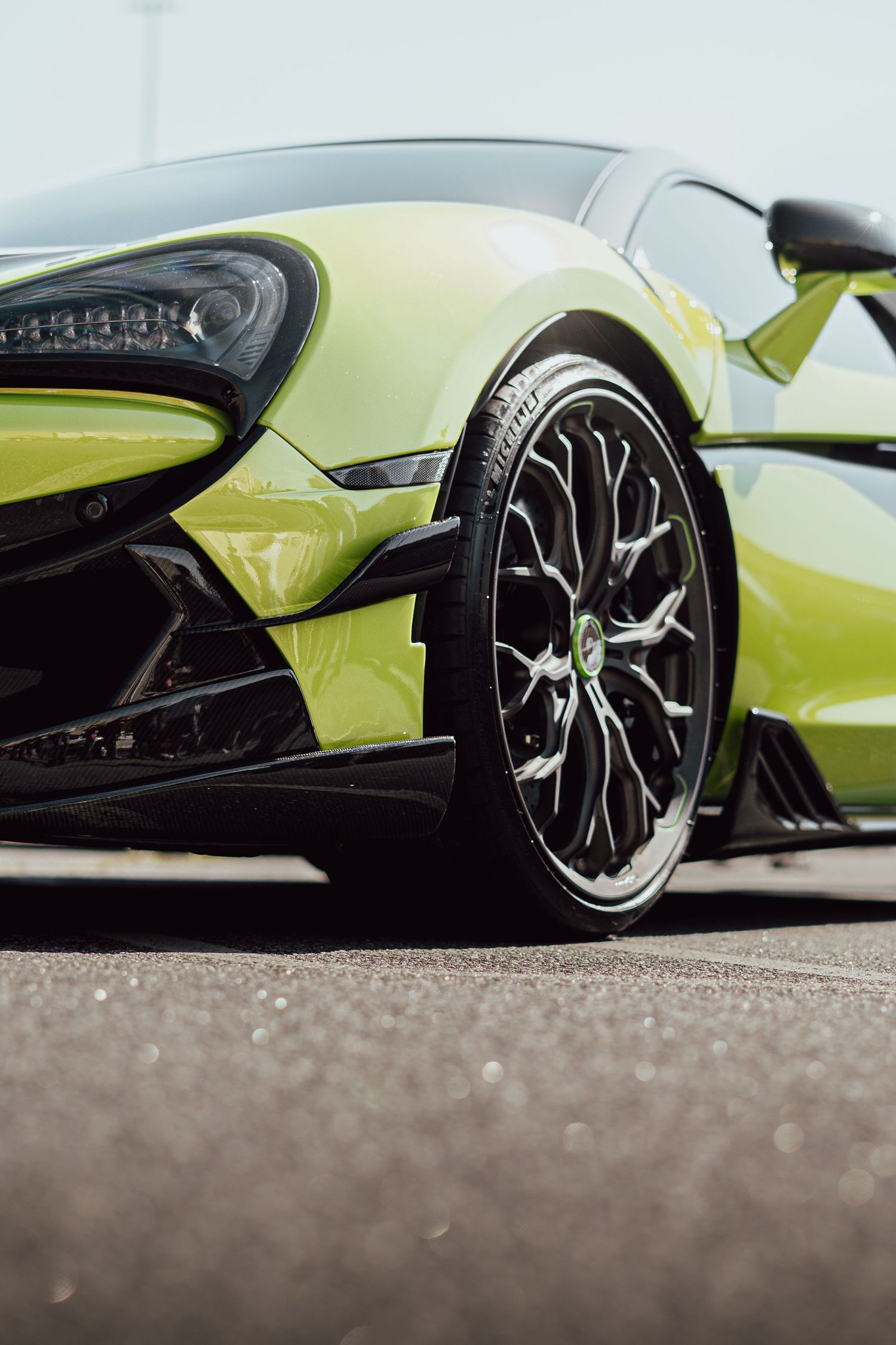 Low angle shot of a neon green McLaren's custom wheels and carbon fiber bodywork.