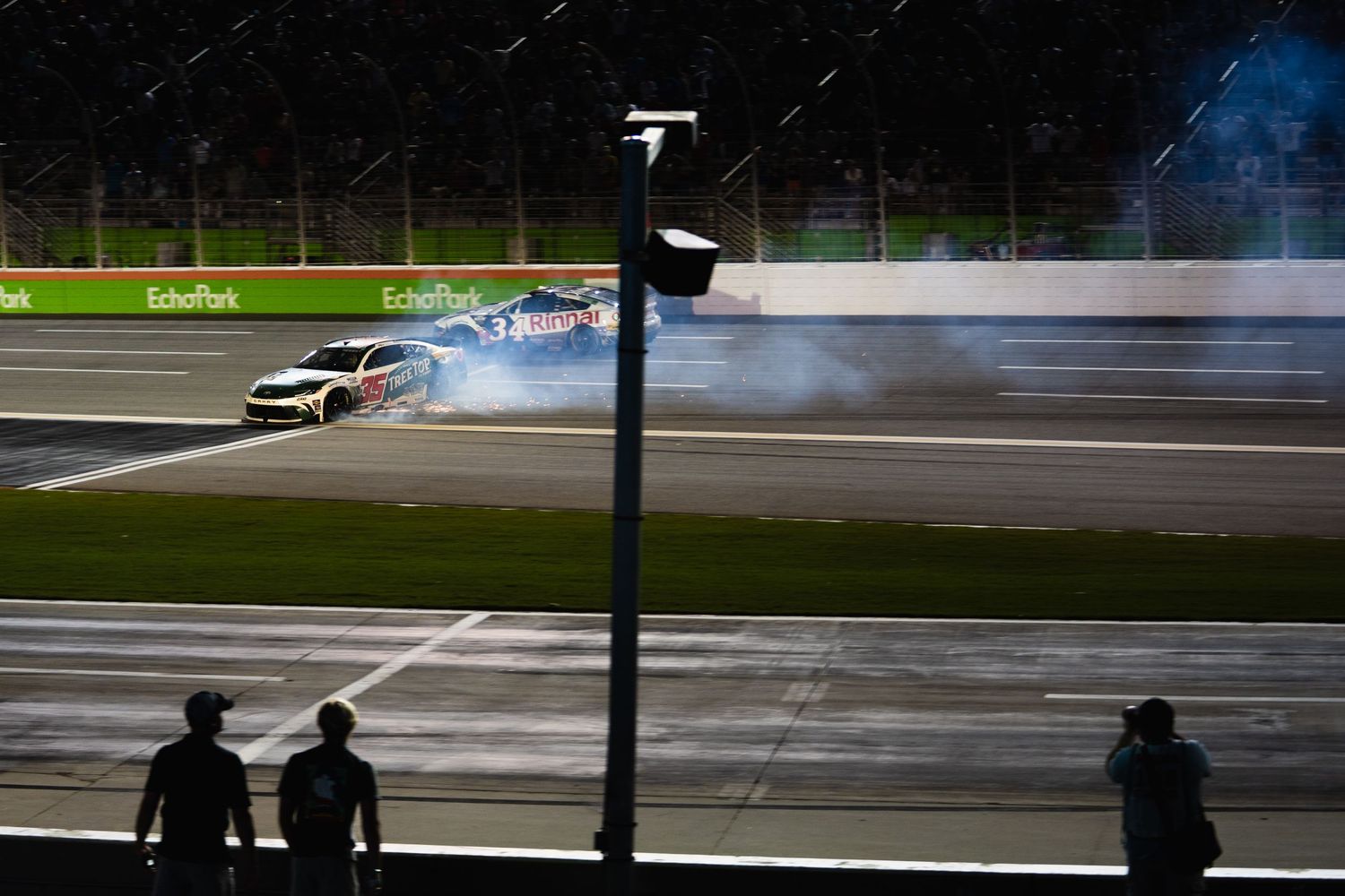 Race car drifts around track corner creating smoke and tire marks during motorsport competition.