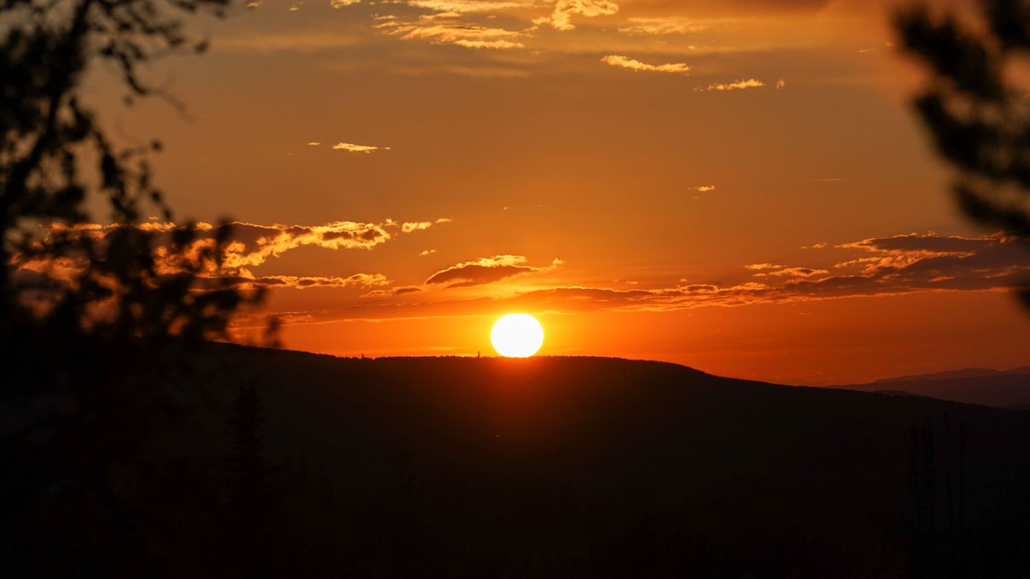 Panoramic sunset view with orange sky and silhouetted horizon.