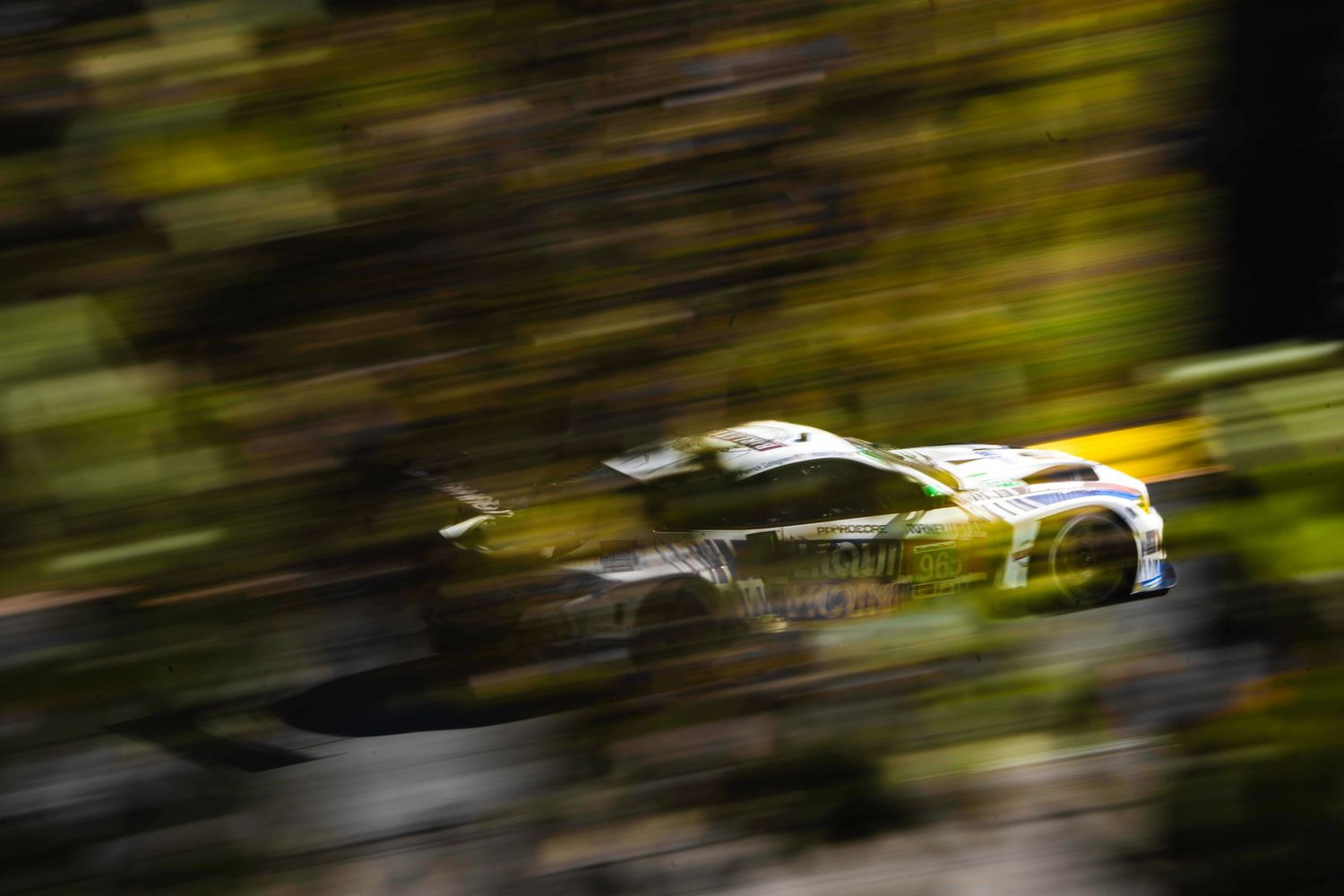 Racing cars in motion blur against green foliage background.