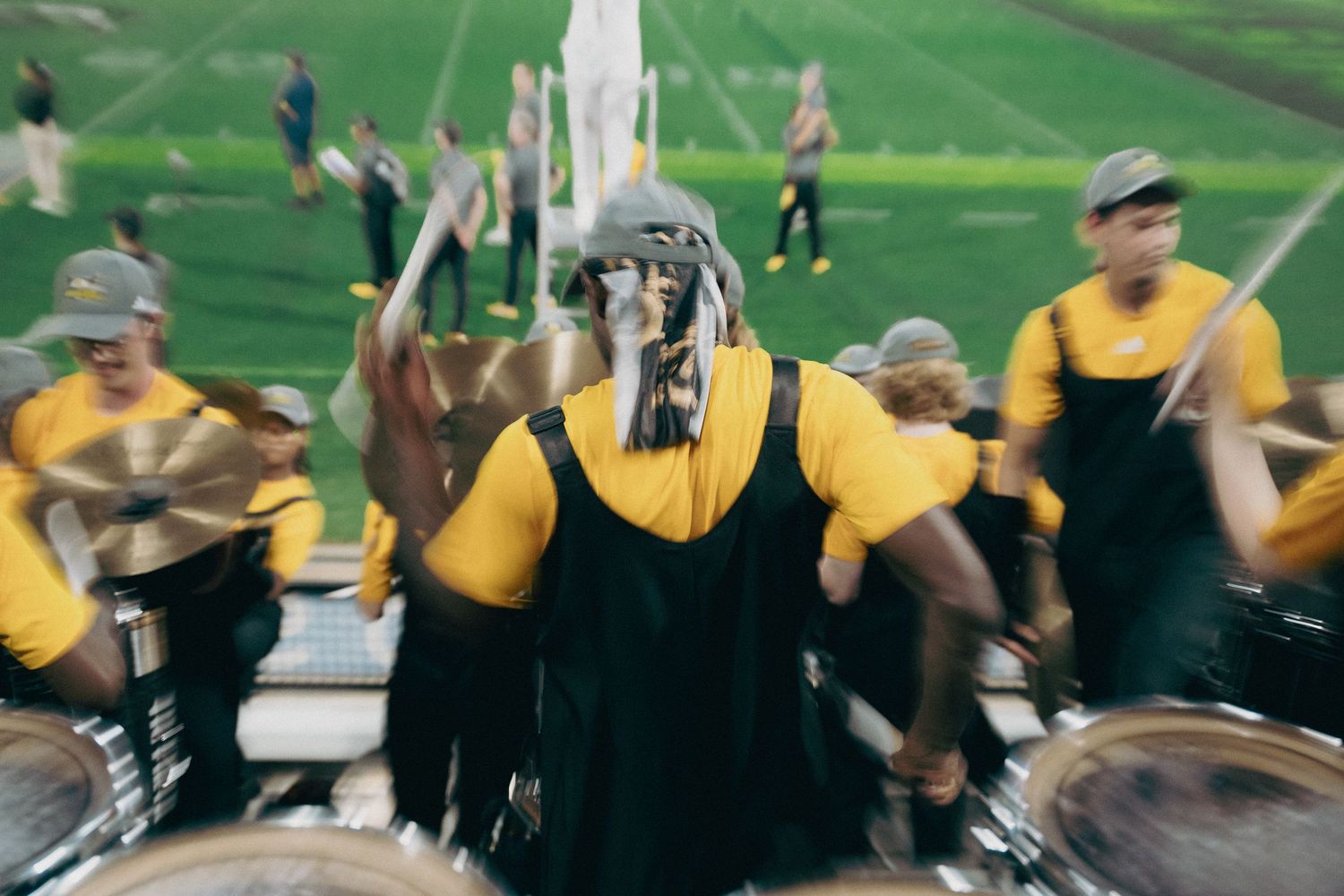 Marching band performers in yellow uniforms create geometric patterns on a green field.