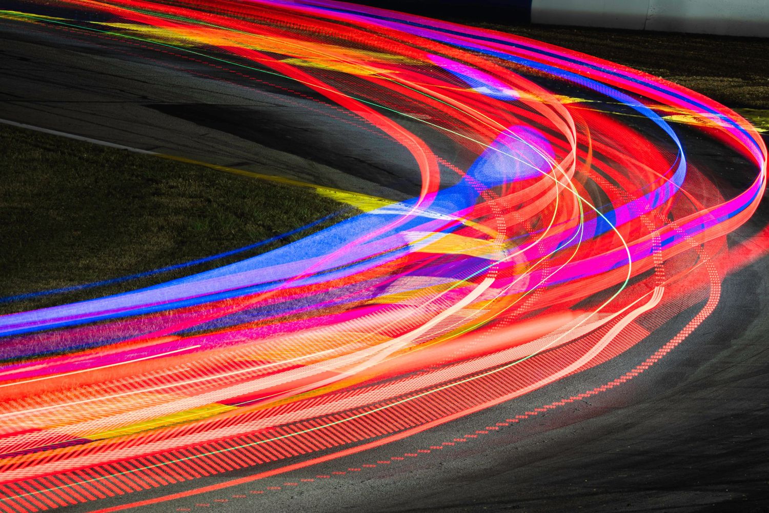 Long exposure photograph captures colorful light trails from race cars on night circuit.