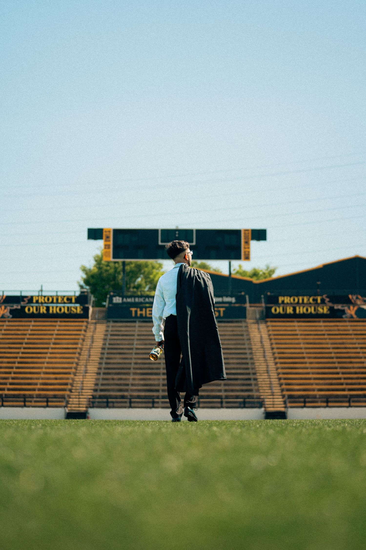 Graduates walking across empty stadium field with bleachers in background.