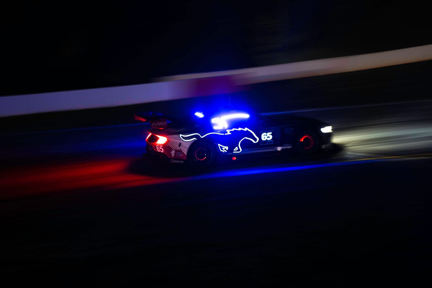 Long exposure shot of race cars at night showing dramatic light trails on dark track.