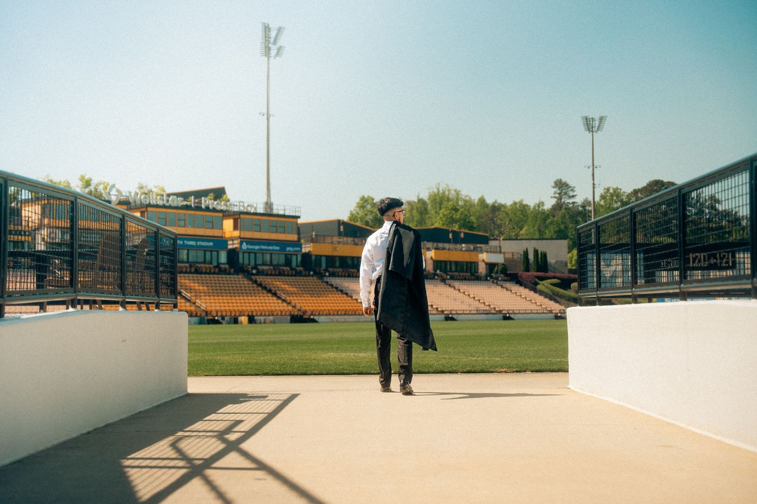 Graduate in cap and gown standing alone overlooking empty stadium bleachers.