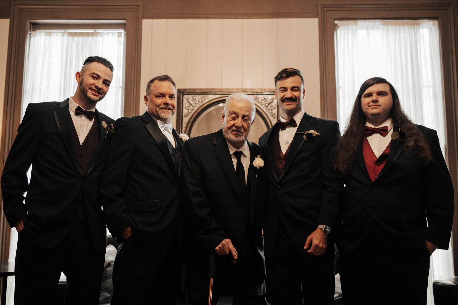 Groomsmen in black suits and bow ties pose together at wedding.