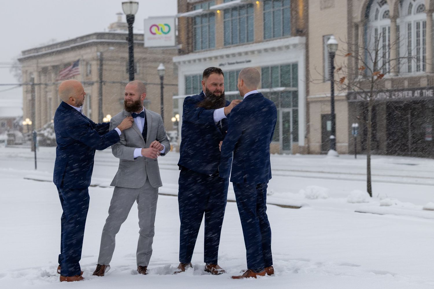 Four men in suits standing in snow outside a building during a winter snowstorm.