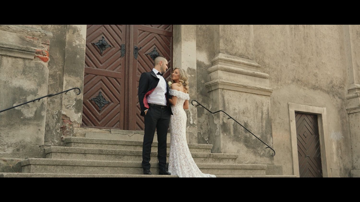 Romantic moment captured against historic stone building with wooden doors.
