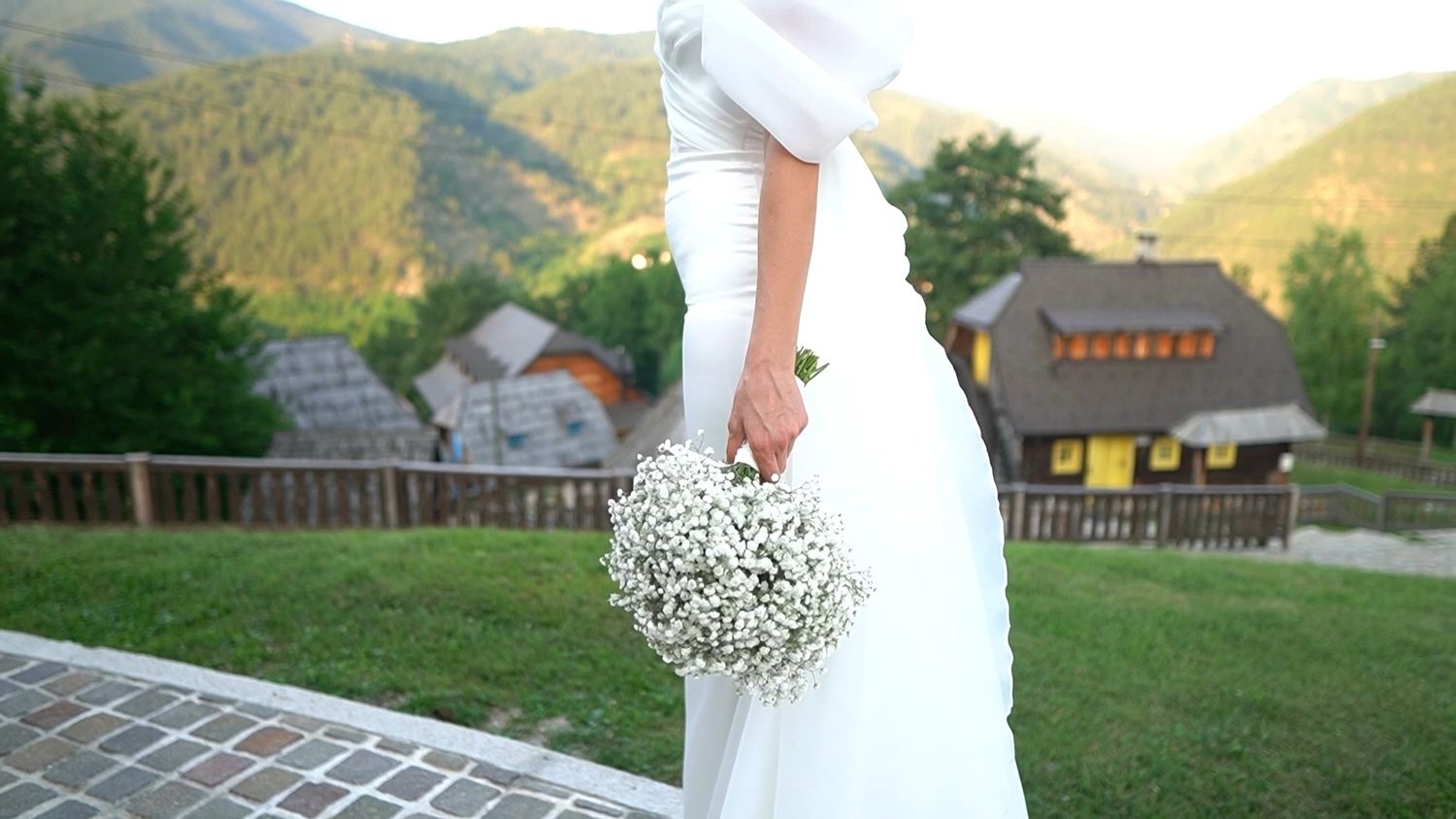 Wedding couple posing in mountain landscape with rustic buildings and sunset lighting.