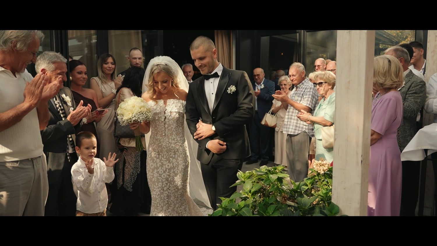 Wedding party and guests celebrate during outdoor garden reception.