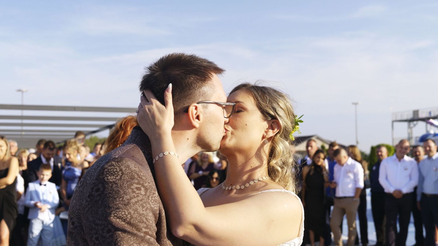 Wedding celebration outdoors with guests gathered under blue sky.