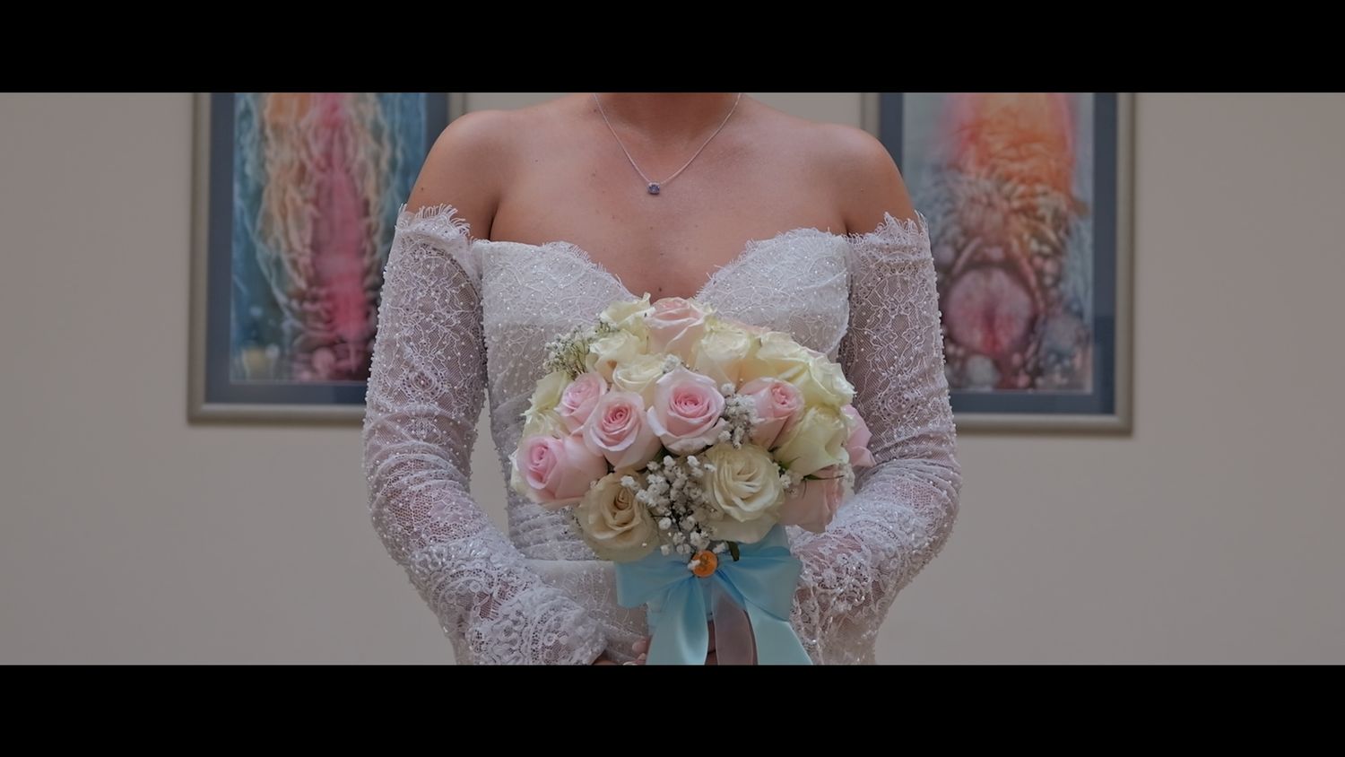 Close-up of bride holding pink and white rose bouquet against neutral background.