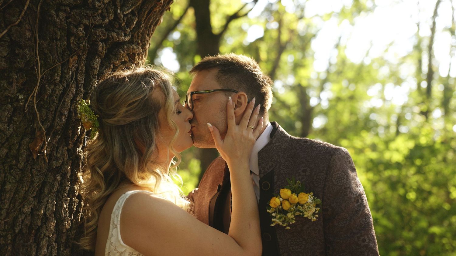 Intimate moment captured in sunlit forest setting during wedding ceremony.