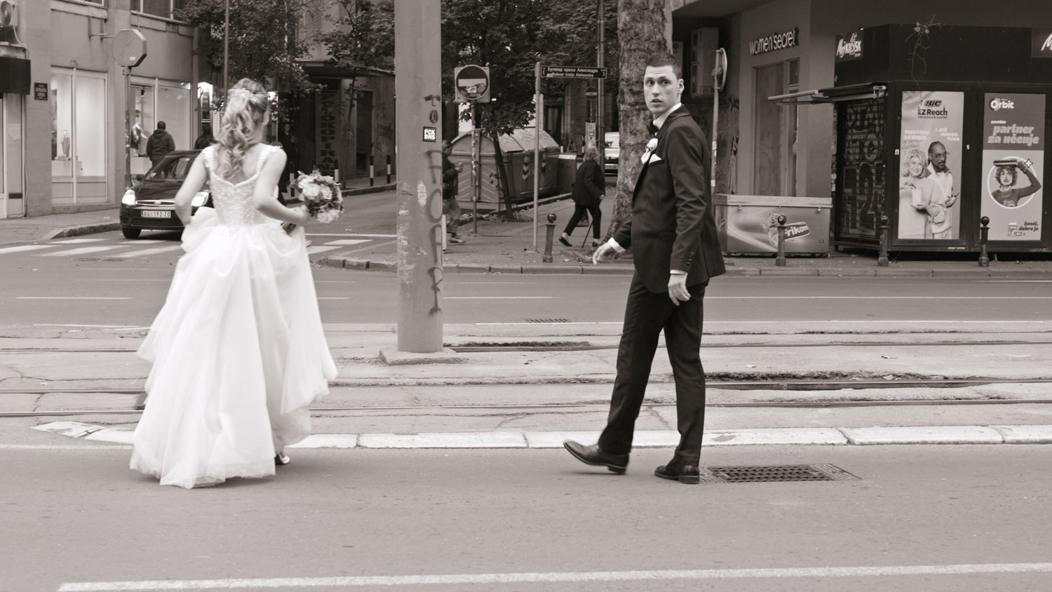 Black and white photo of couple in wedding attire standing on city street.