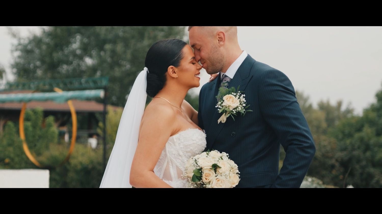 A romantic wedding couple shares an intimate moment outdoors surrounded by lush greenery and natural lighting.