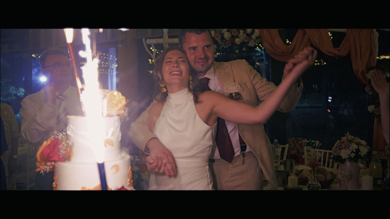 People dancing and celebrating at a lively party with sparklers and string lights overhead.